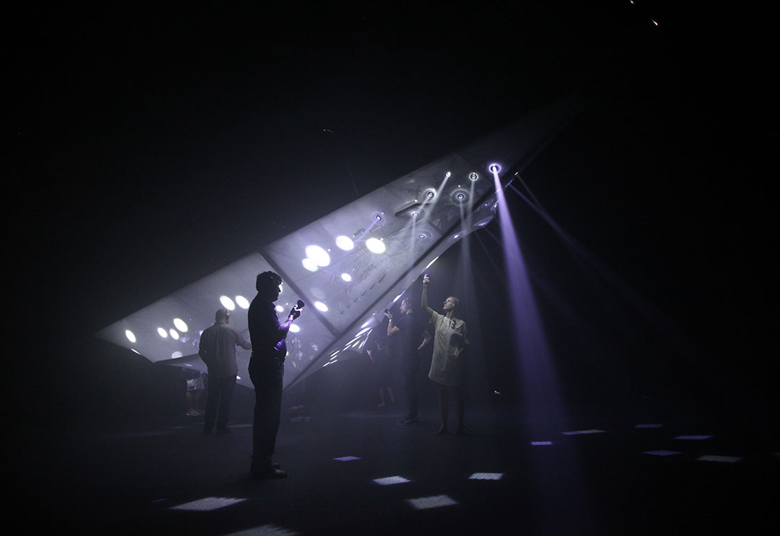 A dark room with people looking at lights in the shape of a plane