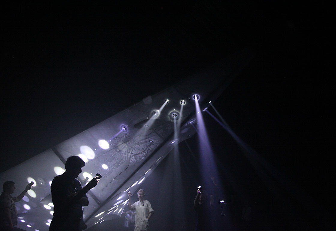 A dark room with people looking at lights in the shape of a plane