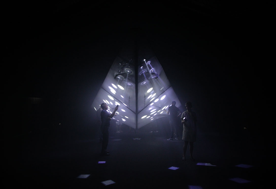 A dark room with people looking at lights in the shape of a plane